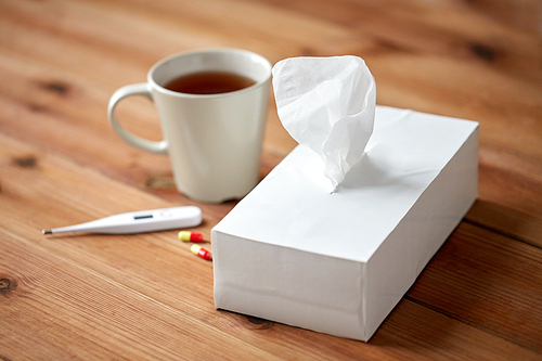 healthcare, medicine, flu and treatment concept - cup of tea, paper wipes and thermometer with pills