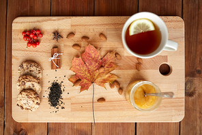 autumn and ethnoscience concept - cup of lemon tea and honey on wooden board with maple leaf, cookies and almond