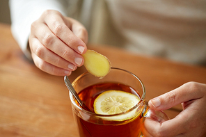 health, traditional medicine and ethnoscience concept - close up of woman adding ginger to tea cup with lemon