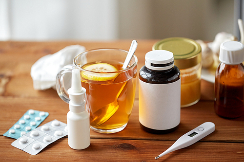 healthcare, traditional medicine and flu concept - cup of tea with lemon, thermometer and drugs on wooden table