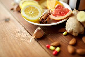 healthcare, traditional medicine and ethnoscience concept - cinnamon, lemon and grapefruit with drug pills on wooden table