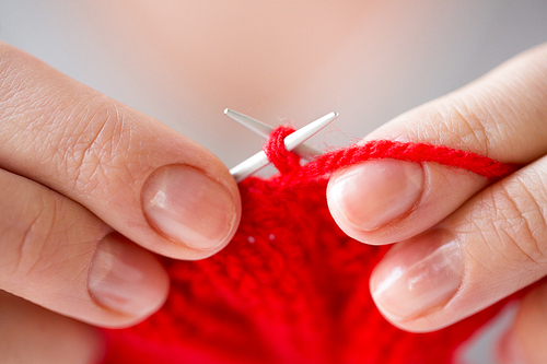 people and needlework concept - close up of woman hands knitting with needles and red yarn