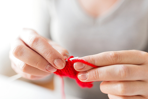 people and needlework concept - close up of woman hands knitting with needles and red yarn