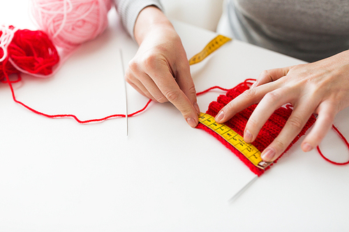 people and needlework concept - woman with measuring tape, knitting, needles and yarn