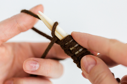 people and needlework concept - close up of woman hands knitting with needles and brown yarn