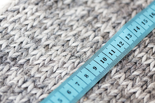 handicraft, knitwear and needlework concept - close up of knitted item with measuring tape