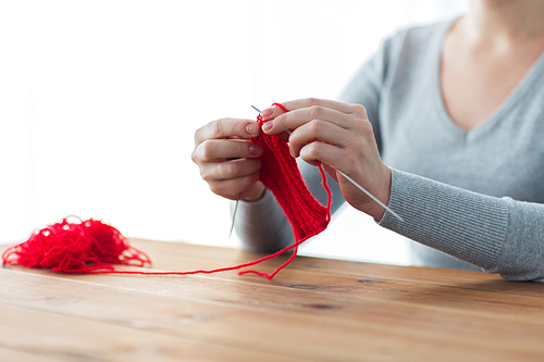 people and needlework concept - woman hands knitting with needles and red yarn