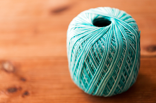 handicraft , knitting and needlework concept - ball of turquoise cotton yarn on wood
