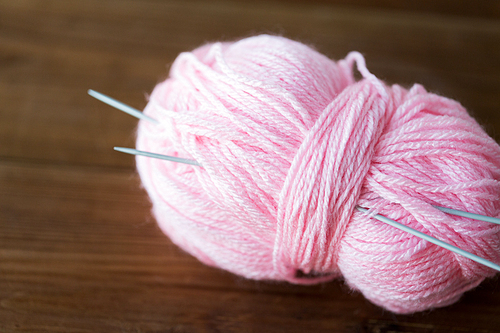 handicraft and needlework concept - knitting needles and ball of pink yarn on wood