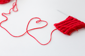 handicraft, love, valentines day and needlework concept - hand-knitted item with knitting needles and thread in heart shape