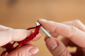 people and needlework concept - close up of hands knitting with crochet hook and red yarn