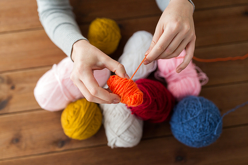 knitting, people and needlework concept - woman pulling yarn up into ball
