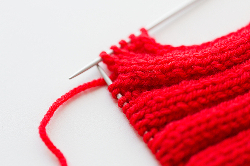 handicraft and needlework concept - close up of hand-knitted item with knitting needles