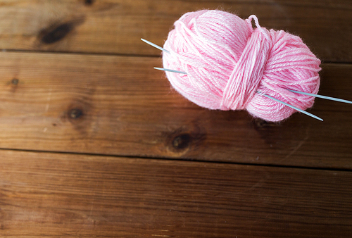 handicraft and needlework concept - knitting needles and ball of pink yarn on wood