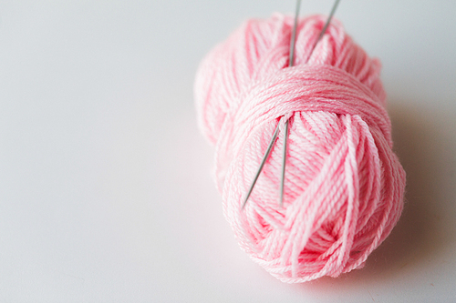 handicraft and needlework concept - knitting needles and ball of pink yarn on white