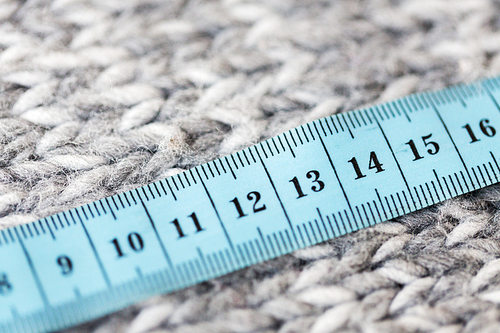 handicraft, knitwear and needlework concept - close up of knitted item with measuring tape