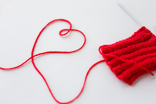 handicraft, love, valentines day and needlework concept - hand-knitted item with knitting needles and thread in heart shape