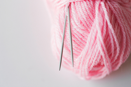 handicraft and needlework concept - close up of knitting needles and ball of pink yarn on white
