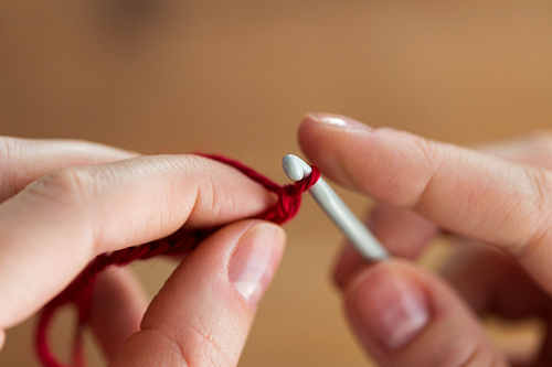 people and needlework concept - close up of hands knitting with crochet hook and red yarn