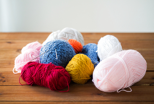 handicraft and needlework concept - knitting needles and balls of yarn on wood