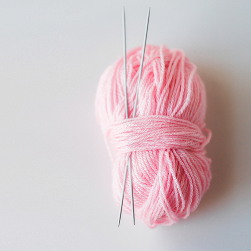 handicraft and needlework concept - knitting needles and ball of pink yarn on white