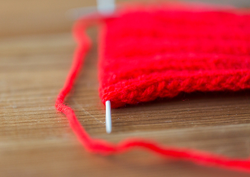 handicraft and needlework concept - hand-knitted item with knitting needles on wood