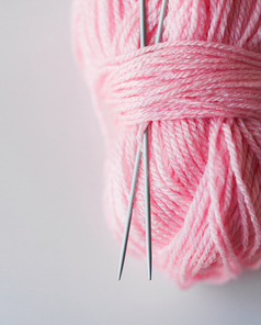 handicraft and needlework concept - close up of knitting needles and ball of pink yarn on white