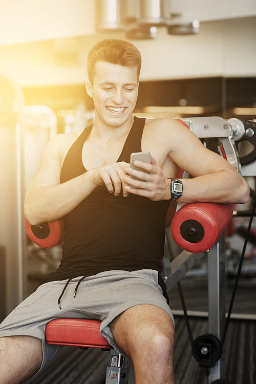 sport, bodybuilding, lifestyle, technology and people concept - smiling young man with smartphone in gym