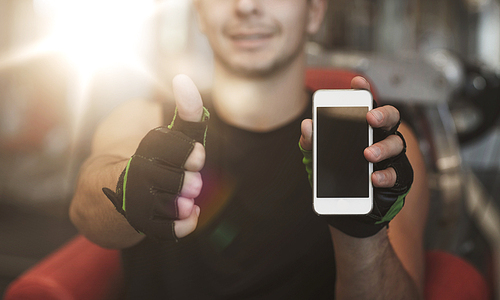 sport, bodybuilding, lifestyle, technology and people concept - happy young man with smartphone showing thumbs up in gym