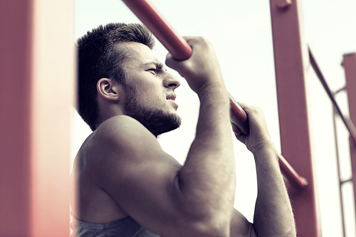 fitness, sport, exercising, training and lifestyle concept - young man doing pull ups on horizontal bar outdoors