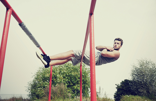 fitness, sport, exercising, training and lifestyle concept - young man doing sit up on parallel bars in summer park