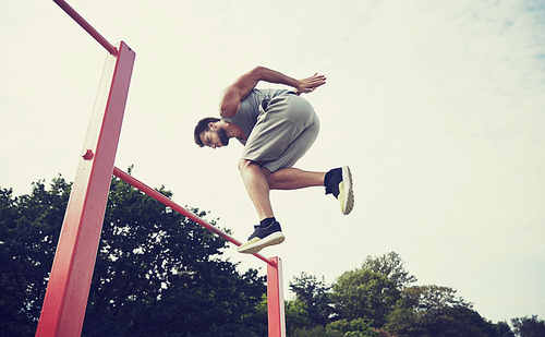 fitness, sport, exercising, training and lifestyle concept - young man jumping on horizontal bar outdoors