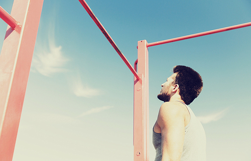 fitness, sport, exercising and lifestyle concept - young man standing and looking at horizontal bar outdoors