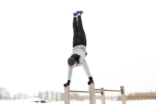 fitness, sport, training, people and exercising concept - young man on parallel bars doing handstand outdoors in winter