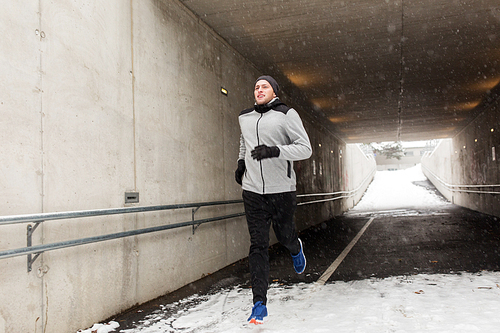 fitness, sport, people, season and healthy lifestyle concept - happy young man running along pedestrian subway tunnel in winter