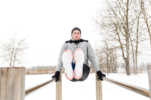 fitness, sport, exercising and people concept - young man doing abdominal exercise on parallel bars in winter