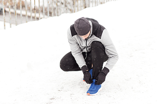 fitness, sport, people, music and healthy lifestyle concept - young man man in earphones tying shoe on winter bridge