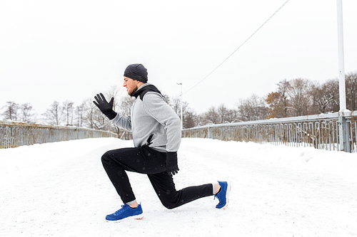 fitness, sport, people, exercising and healthy lifestyle concept - young man doing squats and warming up on snow covered winter bridge