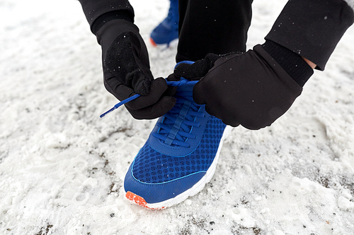 fitness, sport, people, sportswear and footwear concept - close up of man foot and hands tying shoe lace in winter outdoors