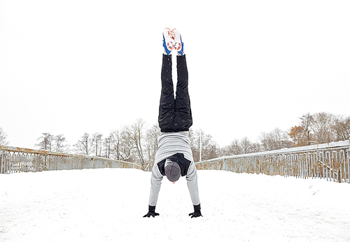 fitness, sport, training, people and exercising concept - young man on doing handstand outdoors in winter
