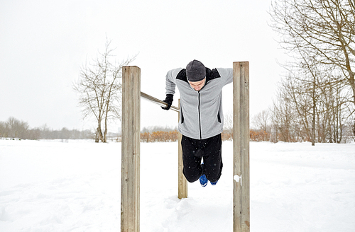 fitness, sport, exercising, training and people concept - young man doing triceps dip on parallel bars outdoors in winter