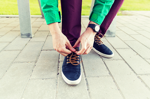 people, footwear and fashion concept - close up of male hands tying shoe laces on street