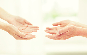 people, age, family, care and support concept - close up of senior woman and young woman reaching hands out to each other