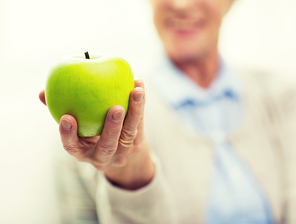 age, healthy eating, food,  and people concept - close up of happy smiling senior woman with green apple at home