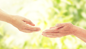 people, age, family, care and support concept - close up of senior woman and young woman reaching hands out to each other over green natural background