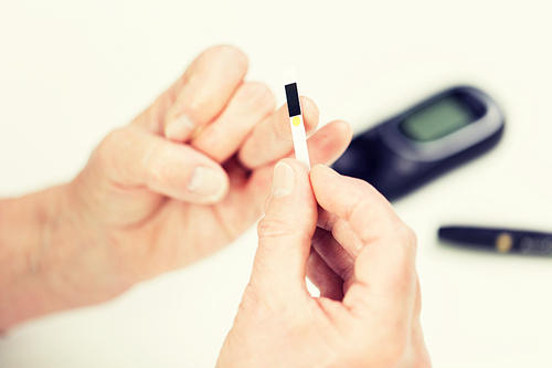 medicine, age, diabetes, health care and people concept - close up of senior woman with glucometer checking blood sugar level at home