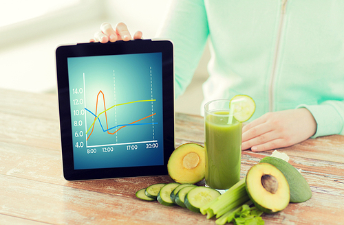 healthy eating, technology, diet and people concept - close up of woman hands holding tablet pc computer with chart, green fresh juice and vegetables sitting at table