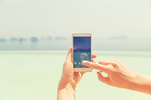 technology, travel, tourism, communication and people concept - close up of male hand holding smartphone on summer beach