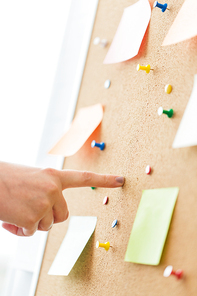 office, business, people and education concept - close up of hand pointing to to cork board with stickers and office pins