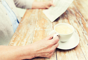 age, leisure and people concept - close up of senior woman drinking coffee and reading newspaper at home